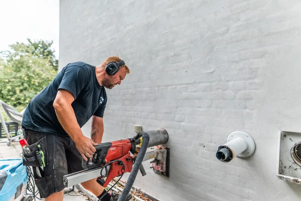 Montör kärnborrar ett runt hål genom en vitmålad yttervägg för ett mini-FTX-aggregat