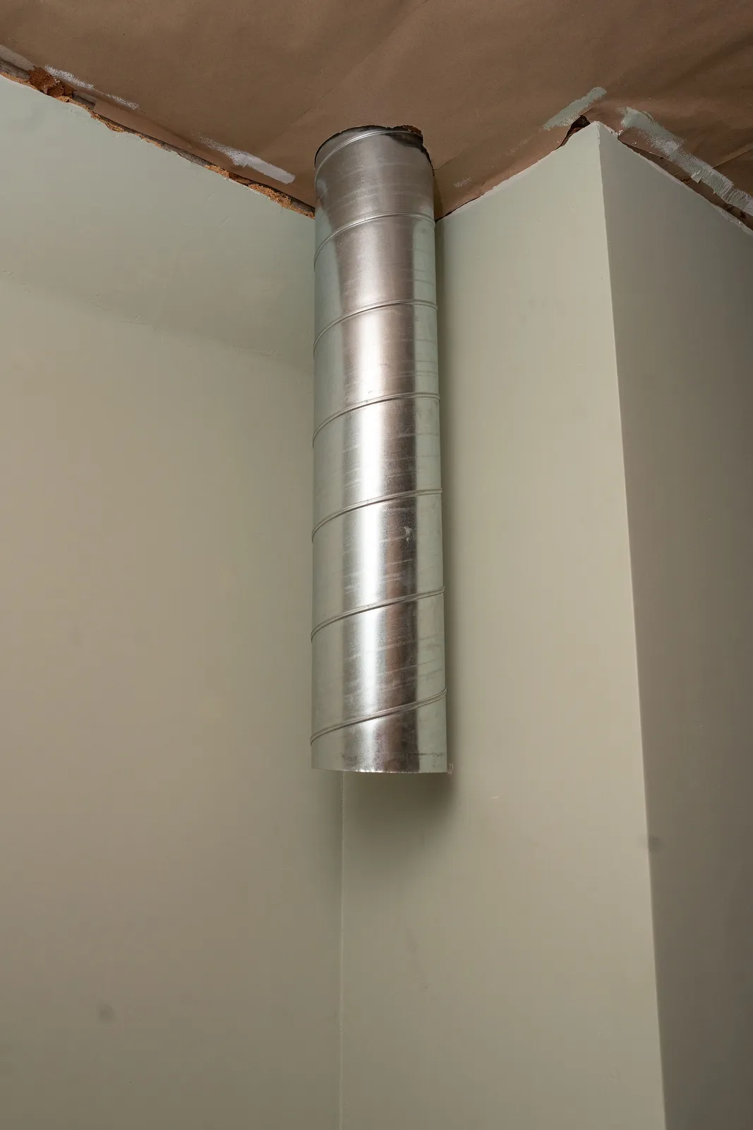 Rund ventilationskanal i galvaniserad plåt som går lodrätt ned från taket i hörnet av ett rum